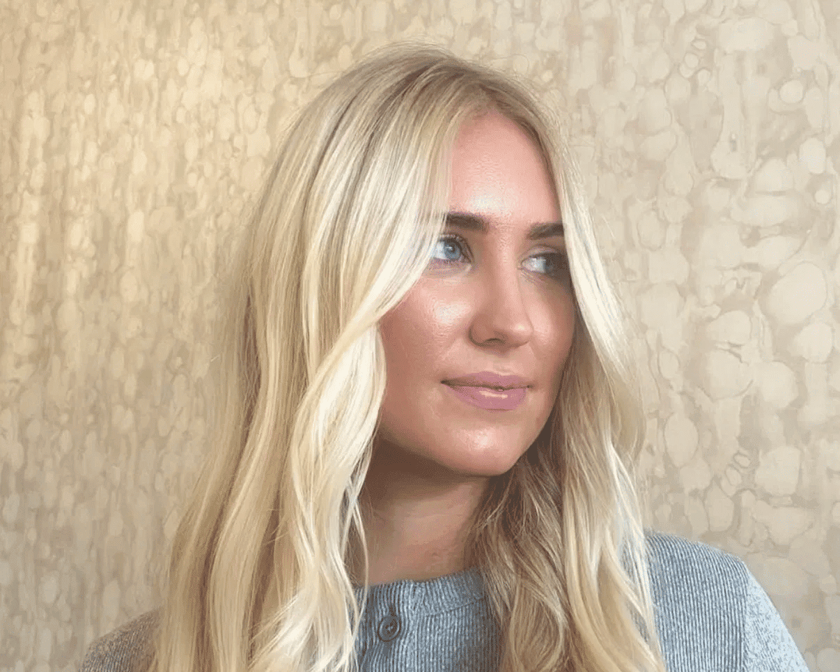 Blonde woman with long hair in a gray shirt, textured wall background.