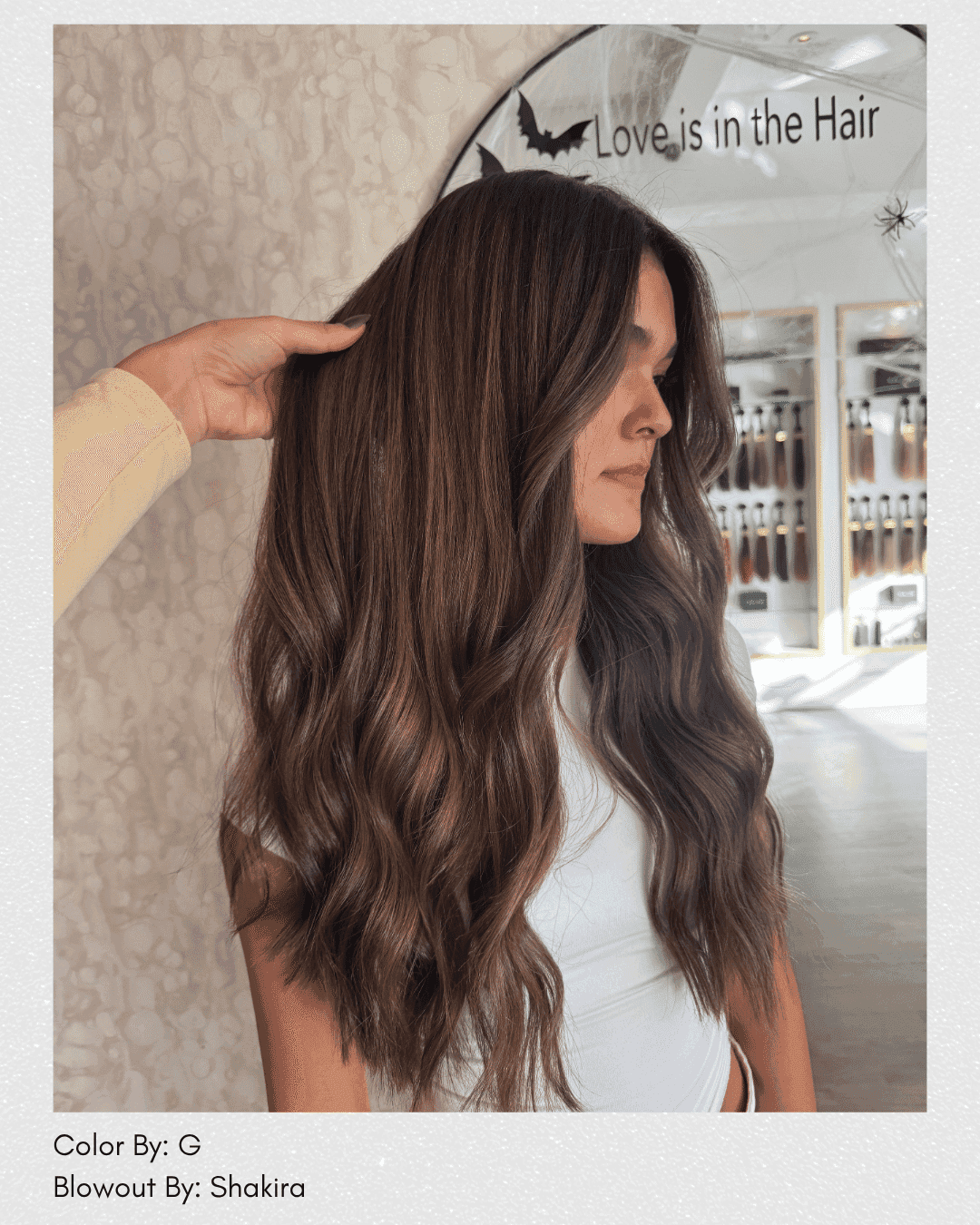 Long, wavy brown hair styled in a salon with hair products in the background.